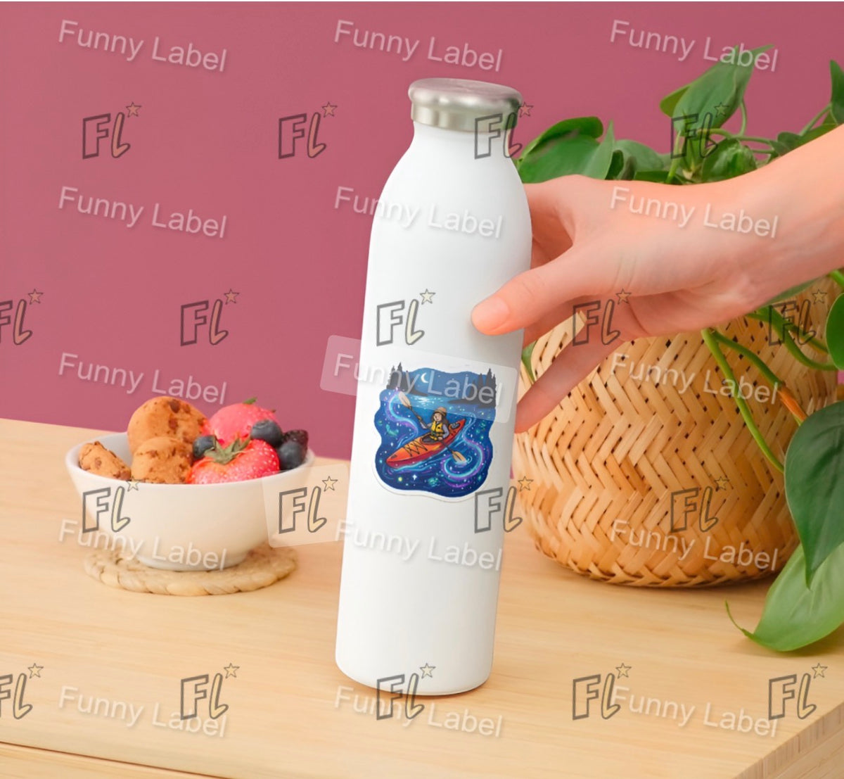 White water bottle with a colorful label held by a hand on a wooden table with a bowl of fruit and a basket of vegetables.