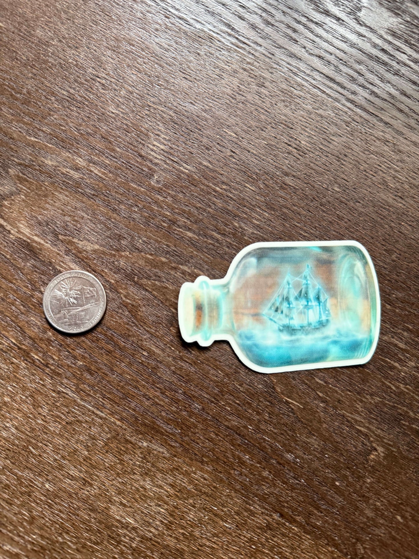 Small glass bottle-shaped object on a wooden surface with a coin for scale.