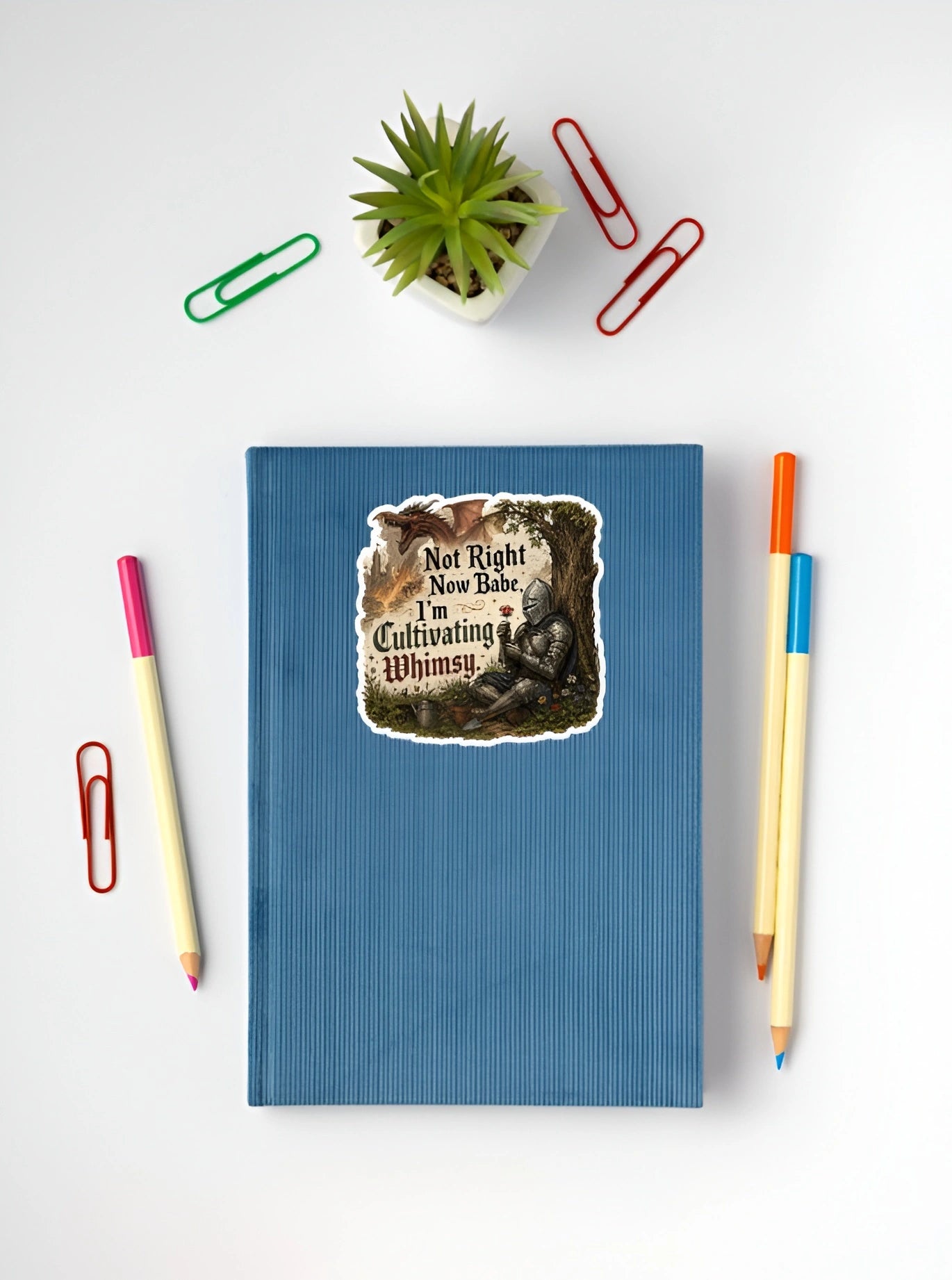 Funny knight sticker reading Not Right Now Babe I’m Cultivating Whimsy on a blue notebook