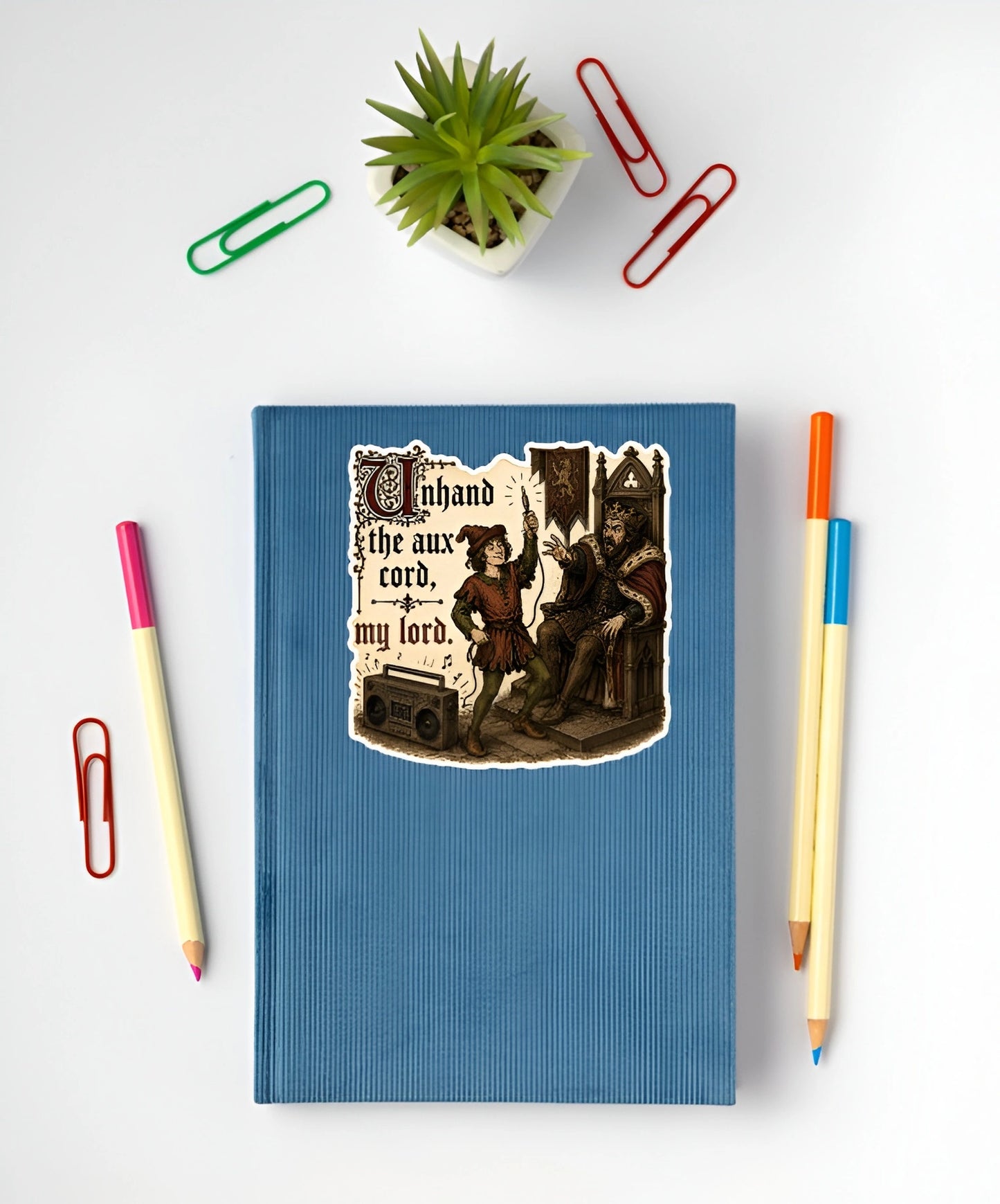 Unhand the Aux Cord My Lord medieval sticker displayed on a blue notebook