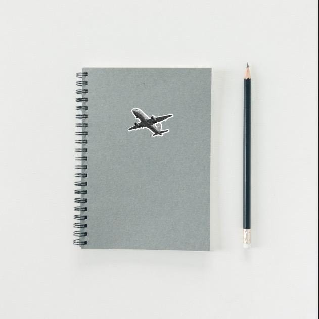 Gray notebook with airplane sticker and a pencil on a light gray background