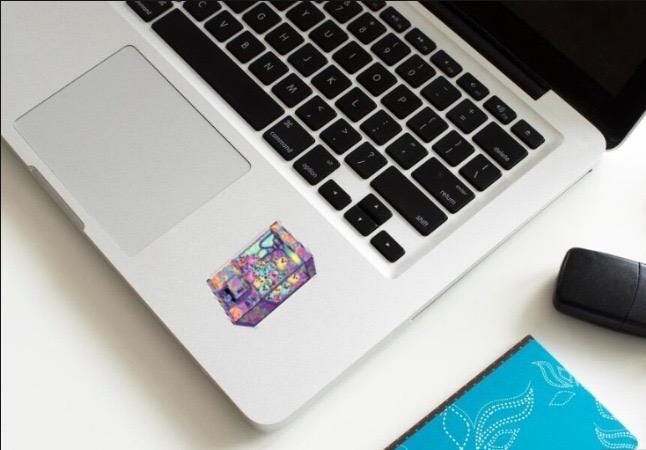 Laptop with a colorful sticker on the palm rest area, next to a mouse and notebook.