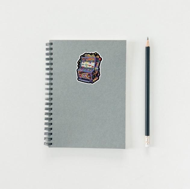 Gray spiral-bound notebook with a colorful slot machine sticker on a white background