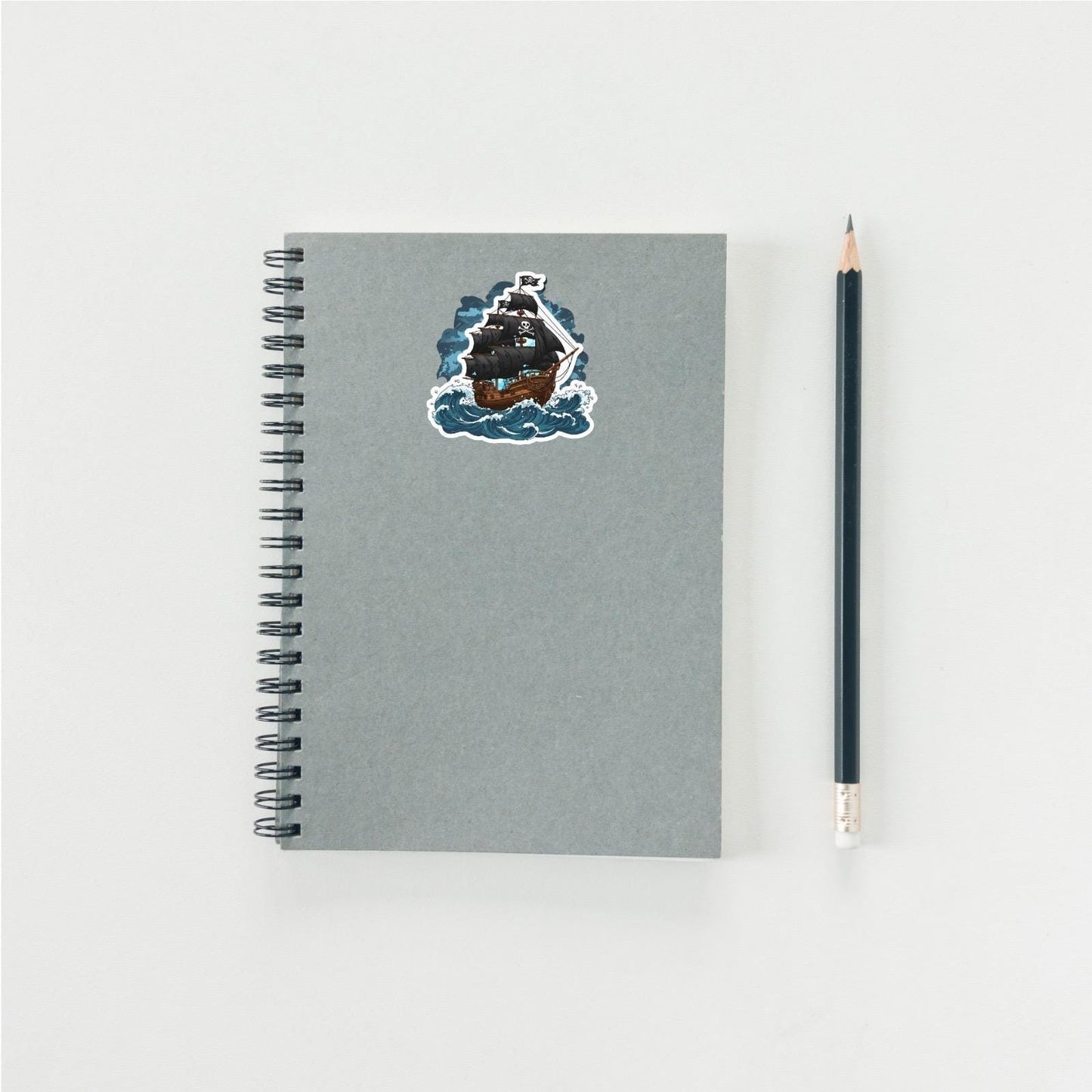 Gray notebook with a pirate ship sticker and a pencil on a light gray background