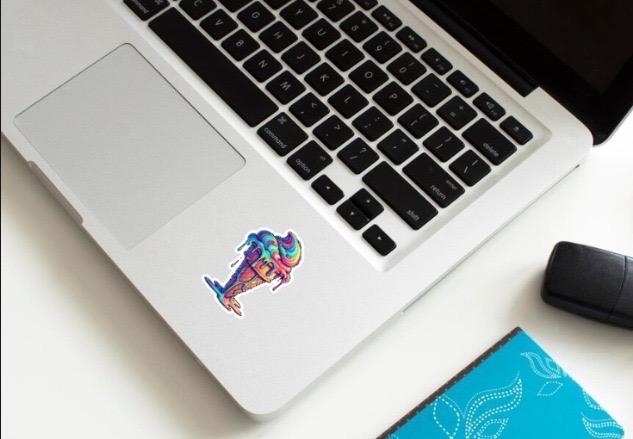 Laptop with a colorful sticker on the palm rest area, next to a mouse and notebook.