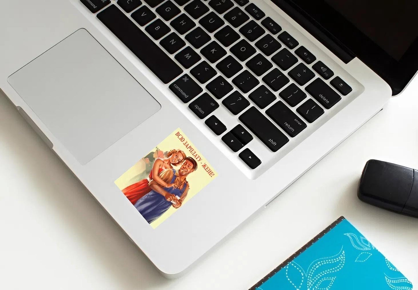 Laptop with a superhero sticker on the palm rest area, next to a mouse and notebook.