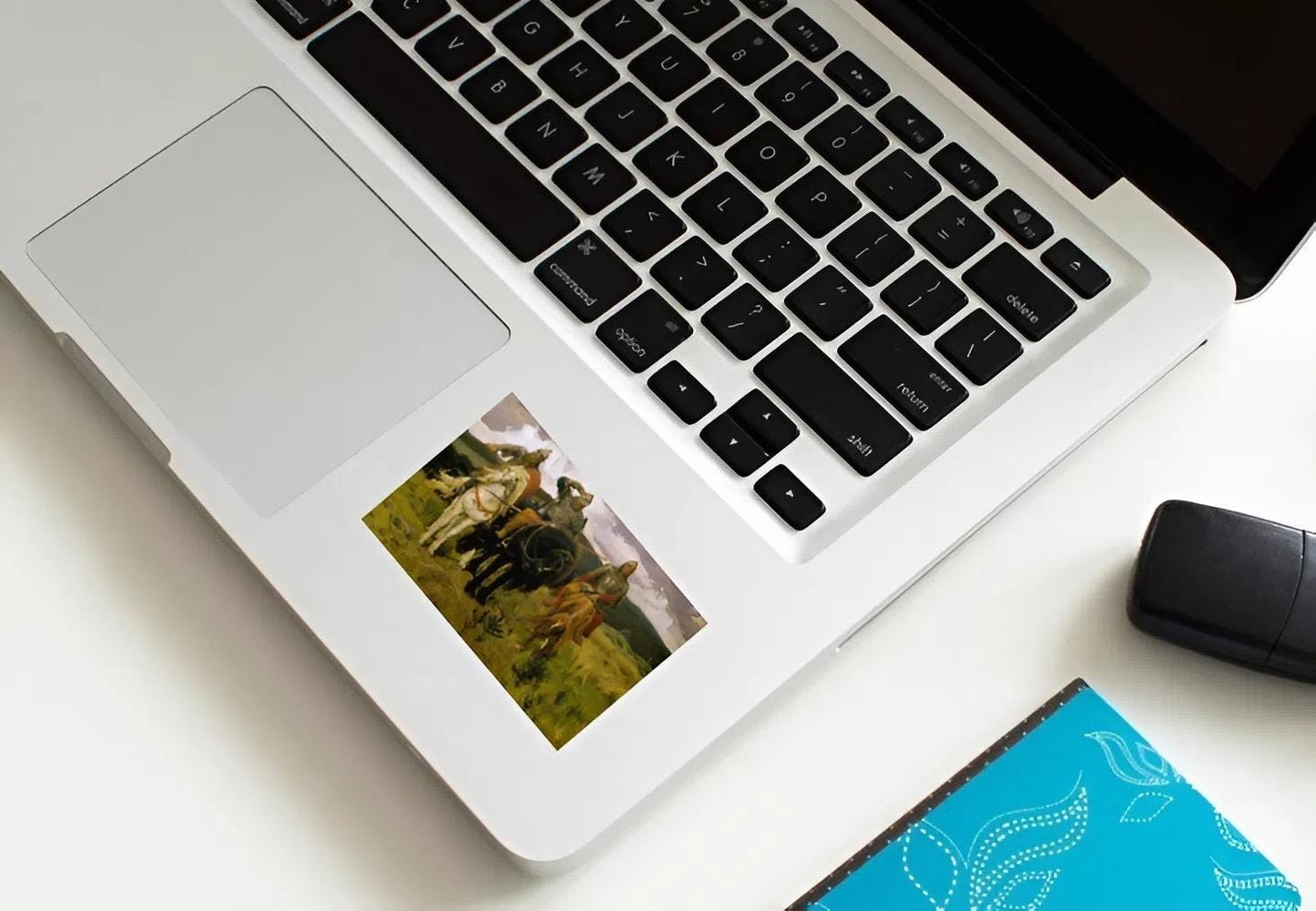 Laptop with a photo of a person on the palm rest area, next to a mouse and notebook.