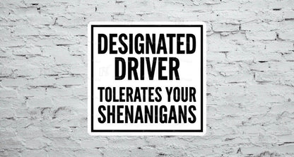 A flat, square vinyl sticker featuring a minimalist black and white sign design with a bold black border enclosing the stacked, high-contrast block text reading "DESIGNATED DRIVER TOLERATES YOUR SHENANIGANS".