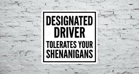 A flat, square vinyl sticker featuring a minimalist black and white sign design with a bold black border enclosing the stacked, high-contrast block text reading "DESIGNATED DRIVER TOLERATES YOUR SHENANIGANS".