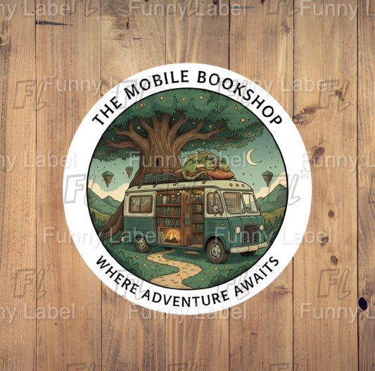 Round sticker of 'The Mobile Bookshop' with a van and tree design on a wooden background.