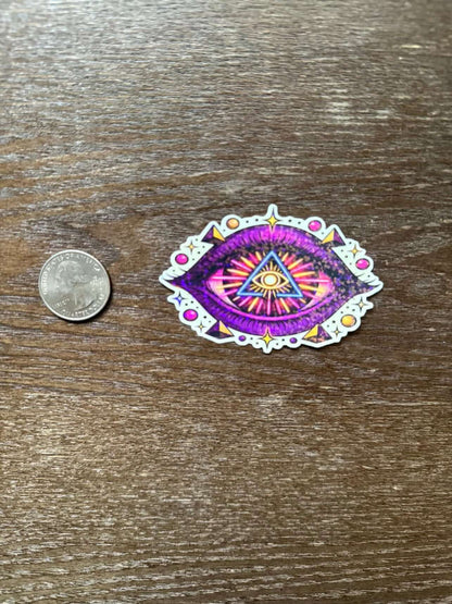 Colorful eye-shaped sticker next to a quarter on a wooden surface