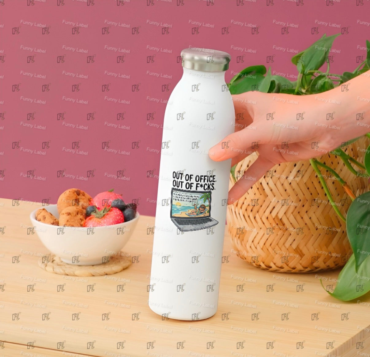 White bottle with a printed design held by a hand on a wooden surface with a bowl of snacks and a plant.