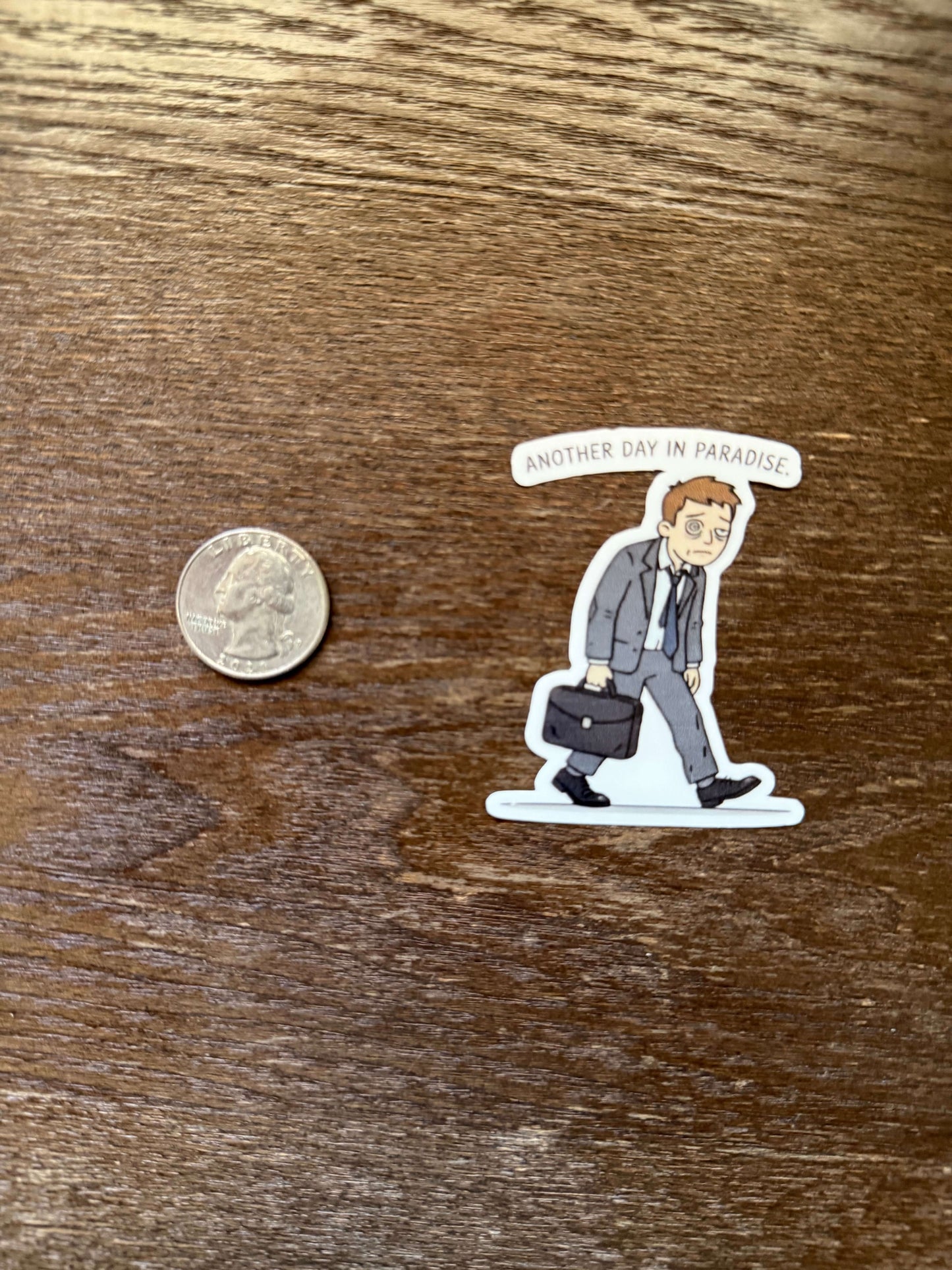 Sticker of a person lying on a bed with a coin for scale on a wooden surface