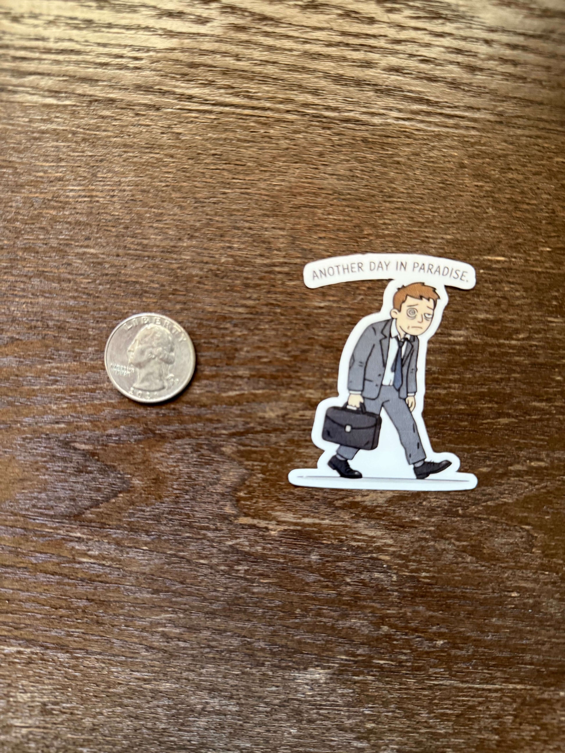 Sticker of a person lying on a bed with a coin for scale on a wooden surface
