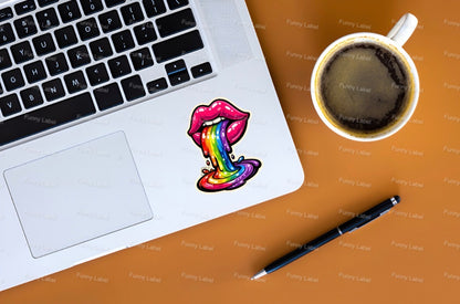 Laptop with a colorful lip design, coffee cup, and pen on a wooden surface.
