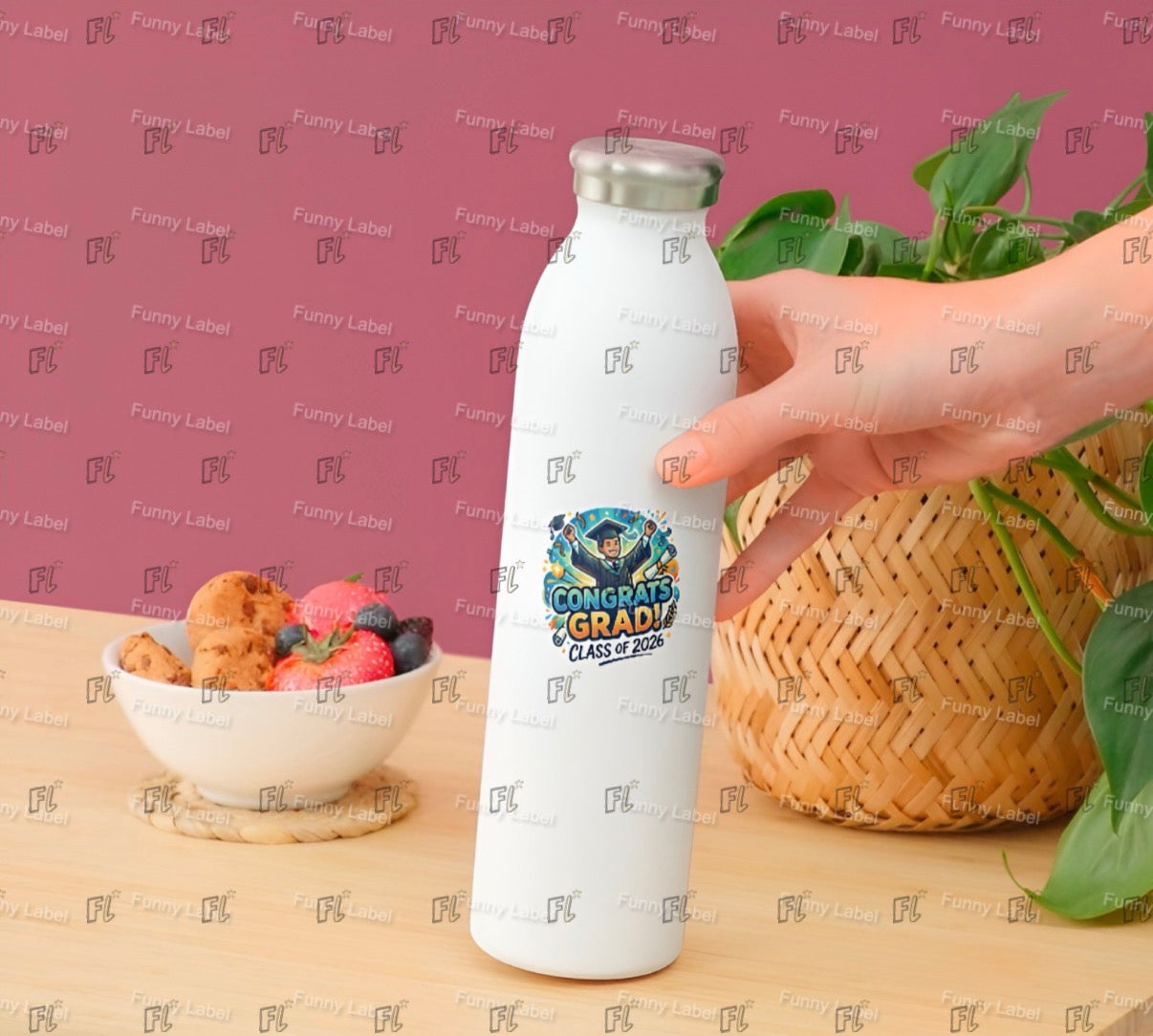 White water bottle with a graduation design held by a hand on a wooden surface with a bowl of snacks and a plant in the background.