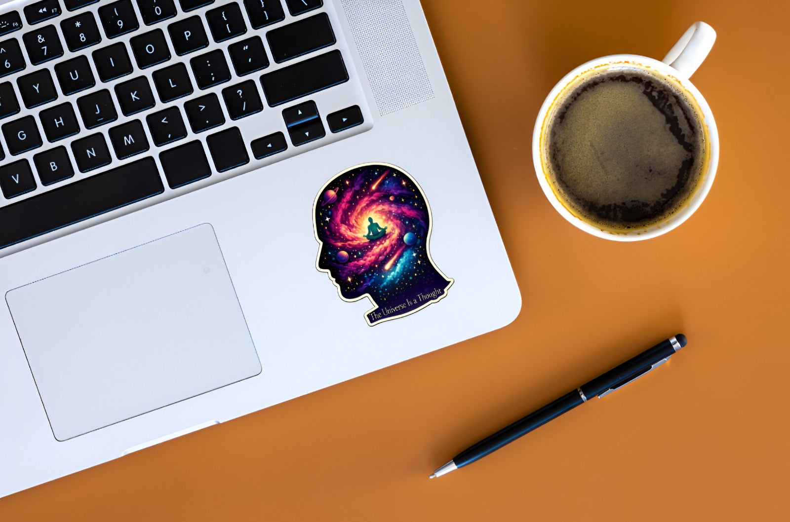 Laptop with a colorful sticker on a desk next to a cup of coffee and pen
