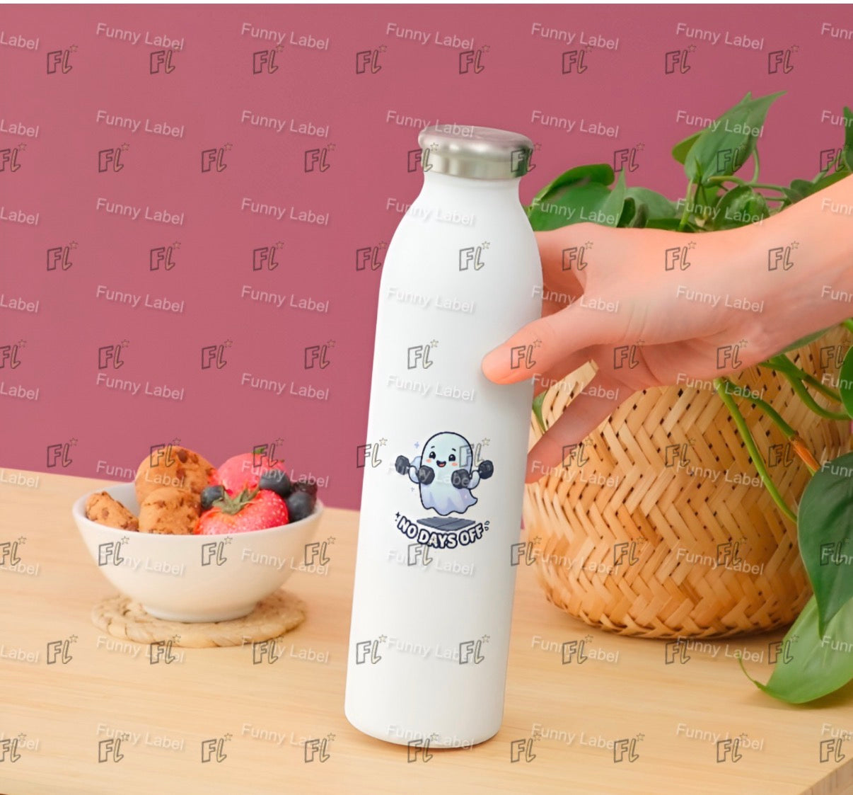 White bottle with a logo held by a hand on a wooden surface with a bowl of fruit and a basket in the background.