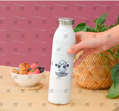 White bottle with a logo held by a hand on a wooden surface with a bowl of fruit and a basket in the background.