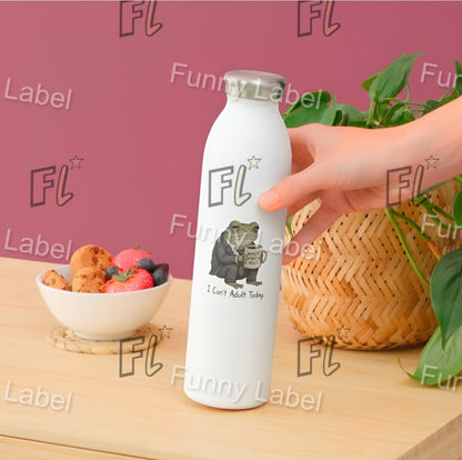 White bottle with 'FL' label held by a hand on a wooden surface with a bowl of fruit and basket in the background.