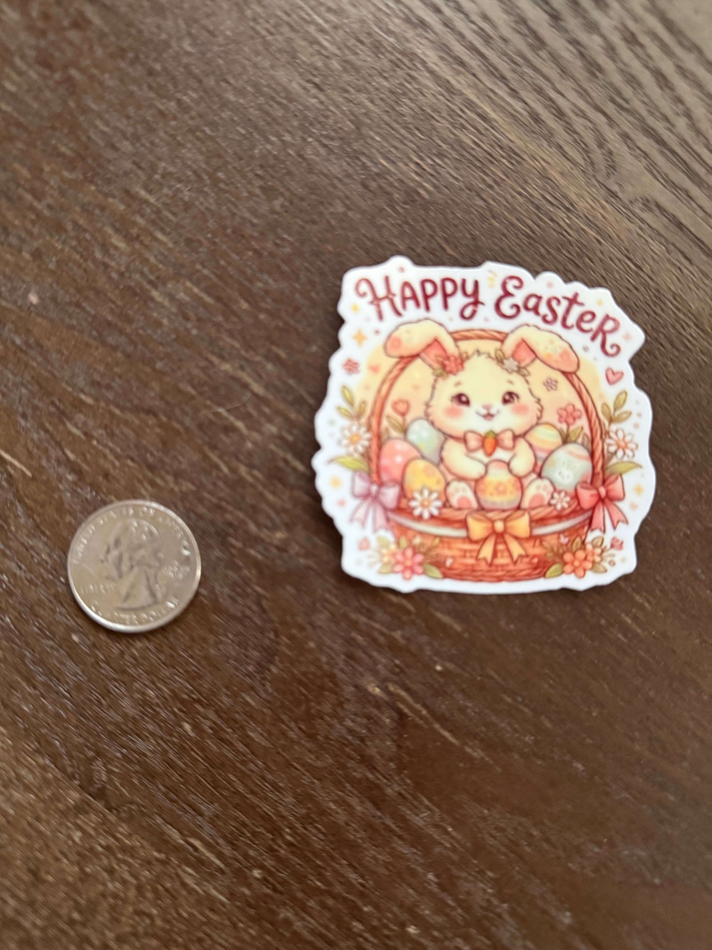 Sticker with 'Happy Easter' text and cartoon bear design on a wooden surface, next to a coin for size comparison.
