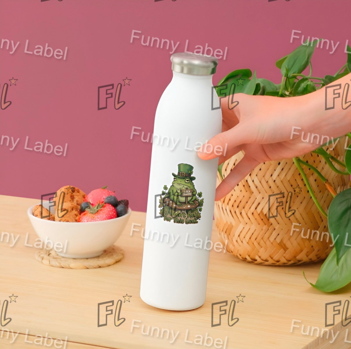 White water bottle with a green character design held by a hand on a wooden table with a bowl of fruit and a plant.