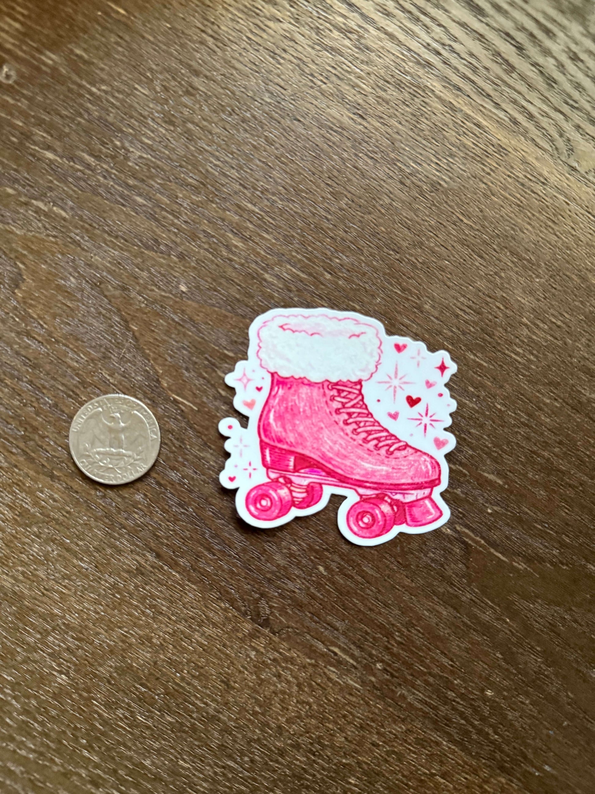Pink roller skate sticker with white details on a wooden surface next to a coin for scale.