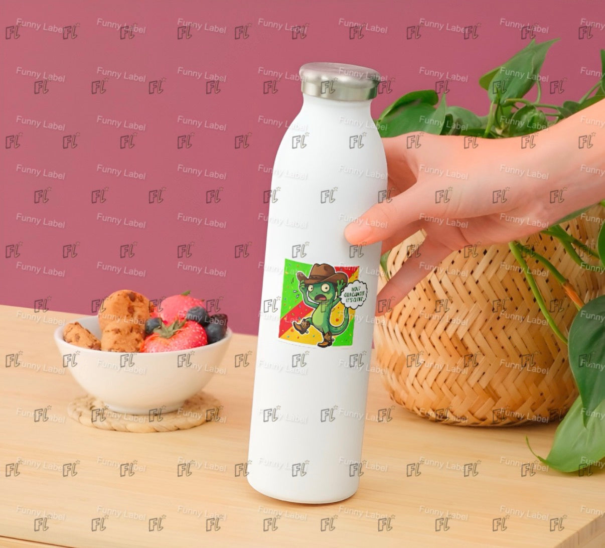 White water bottle with a cartoon character label held by a hand on a wooden surface with a bowl of fruit and basket in the background.