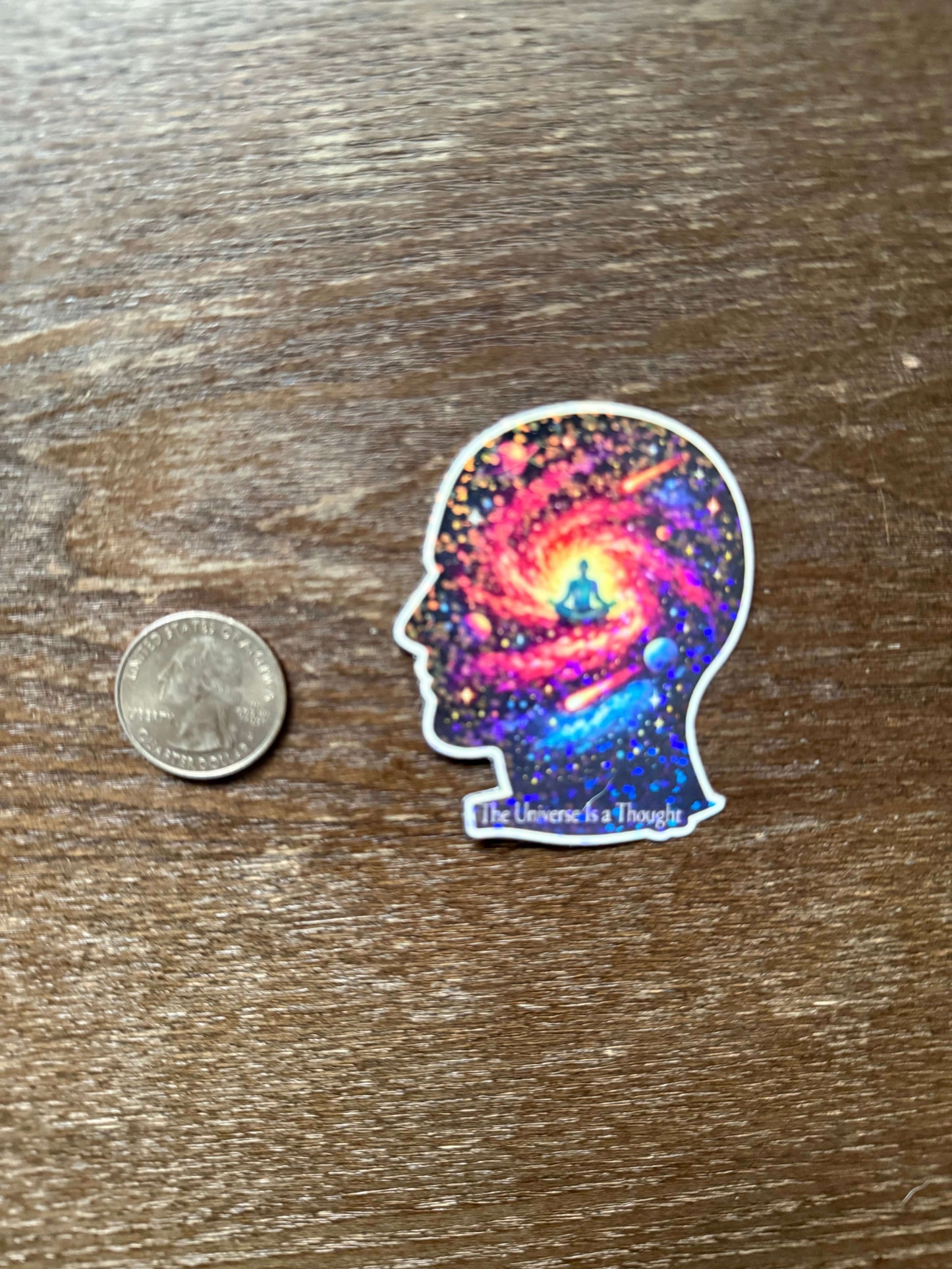 Sticker of a colorful galaxy in a head design next to a quarter on a wooden surface
