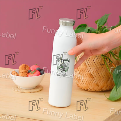 White bottle with 'Funny Label' branding held by a hand on a wooden table with fruit and plants.