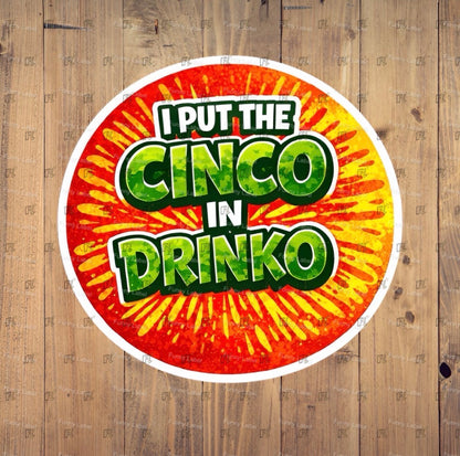 Circular sticker with colorful text 'I PUT THE CINCO IN DRINKO' on a wooden background