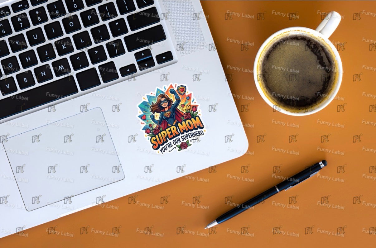 Laptop with a 'Super Mom' sticker, coffee cup, and pen on a brown surface.