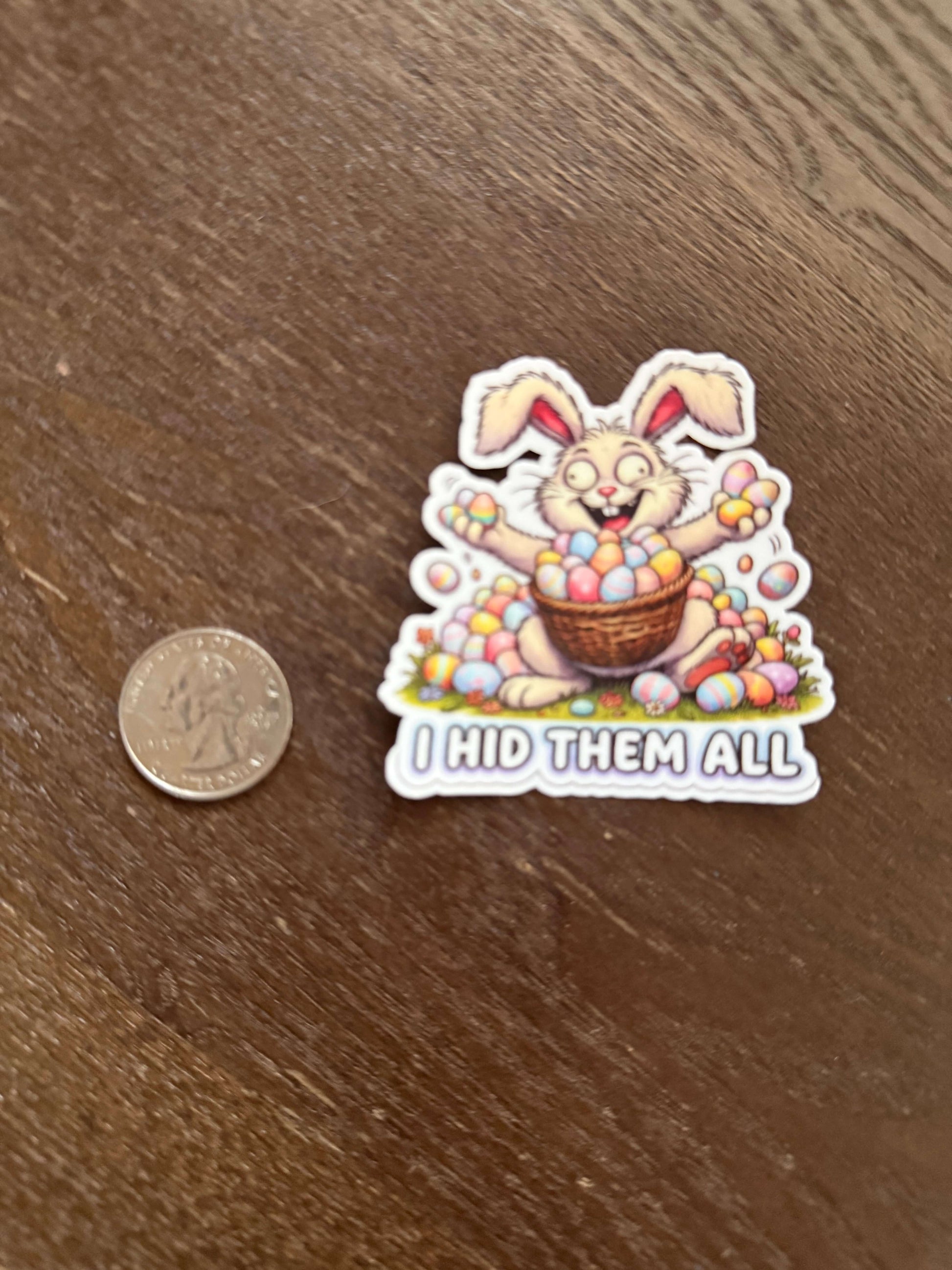 Sticker of a cartoon rabbit with a basket of Easter eggs on a wooden surface, next to a coin for scale.