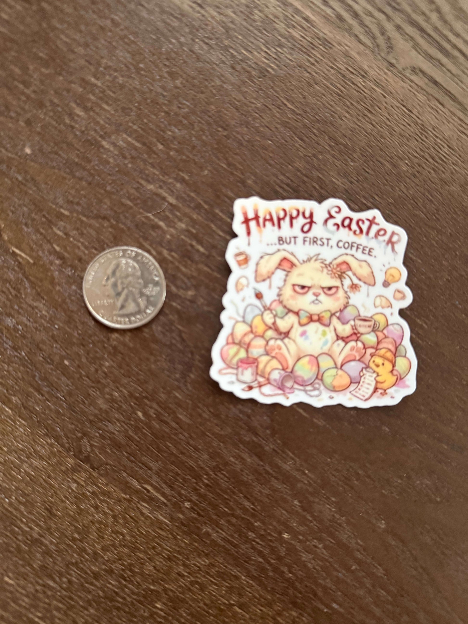 Sticker with Easter design featuring a cat surrounded by eggs, next to a coin for scale on a wooden surface.