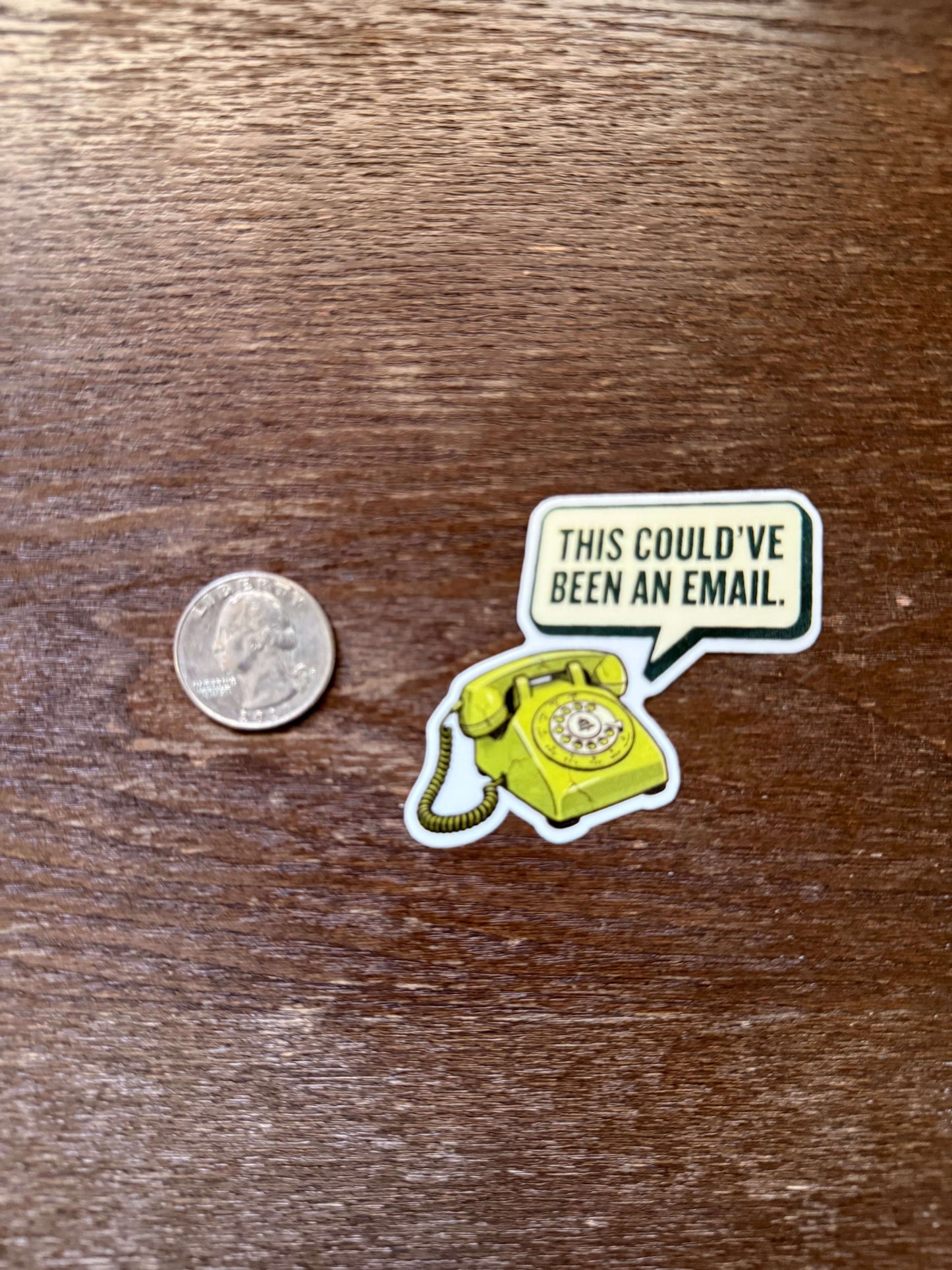 Sticker with a phone graphic and text 'This could've been an email' on a wooden surface.