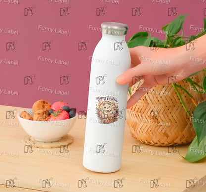 White bottle with Easter design held by a hand on a wooden surface with a bowl of cookies and fruit, and a plant in the background.