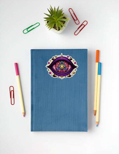 Blue notebook with a decorative eye design on a white background with stationery items.