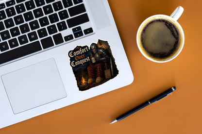 Funny Comfort Over Conquest knight sticker displayed on a silver laptop beside a cup of coffee