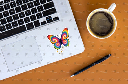 Laptop with a colorful butterfly design on a brown surface next to a cup of coffee and pen.
