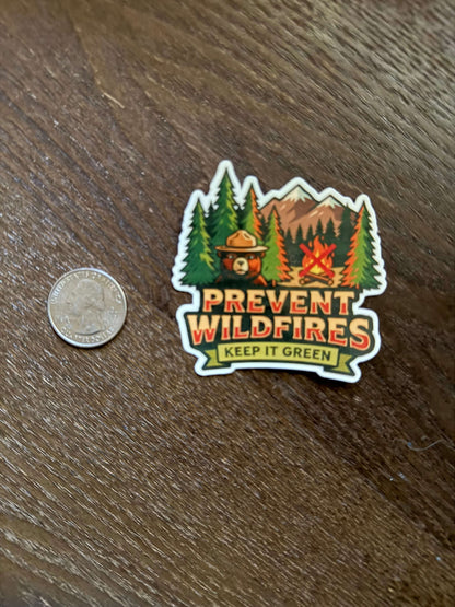 Sticker with wildfire prevention message on a wooden surface next to a coin for scale.