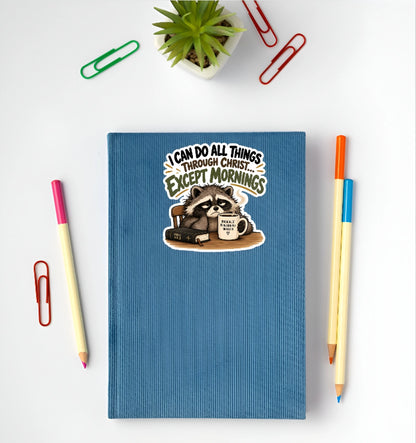 I Can Do All Things Through Christ Except Mornings funny Christian raccoon sticker displayed on a blue notebook