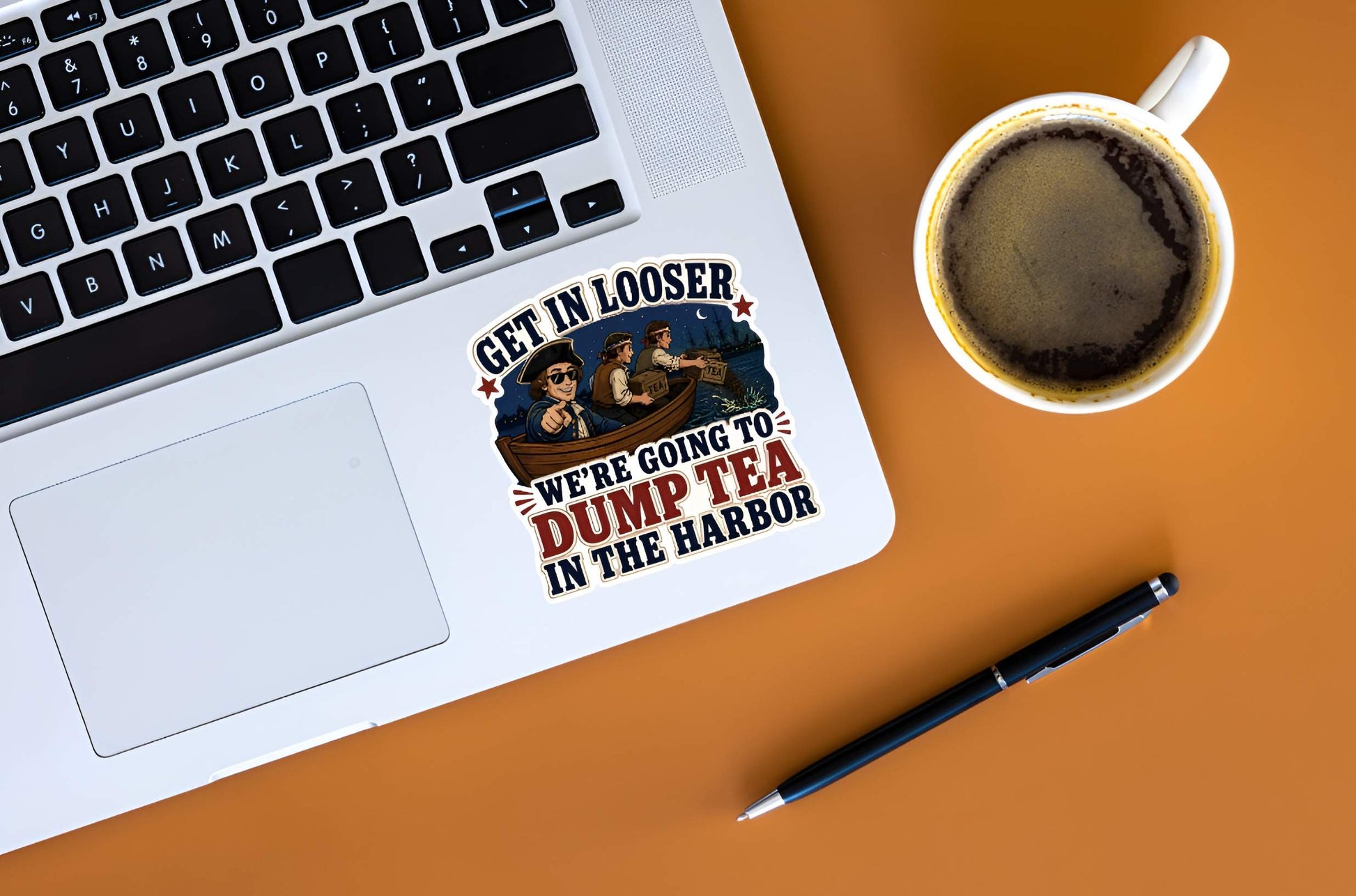 Laptop with a sticker on a desk next to a cup of coffee and pen