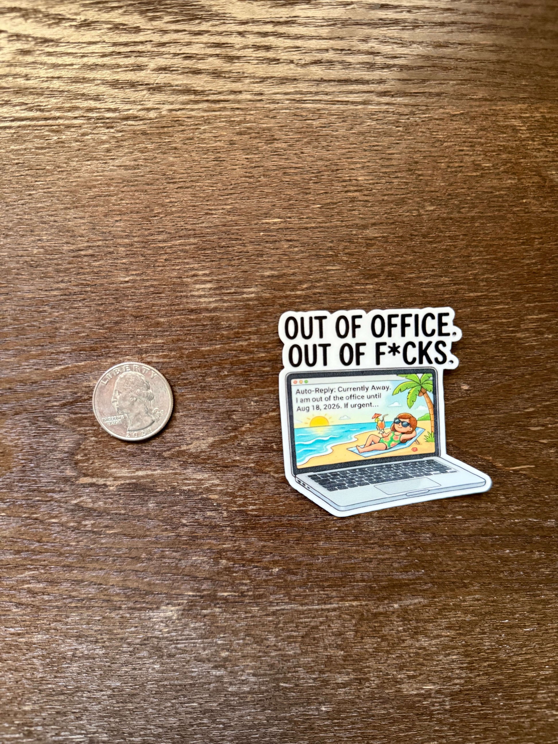 Sticker with laptop graphic and text 'Out of Office: Out of F*cks' on a wooden surface with a coin for scale.