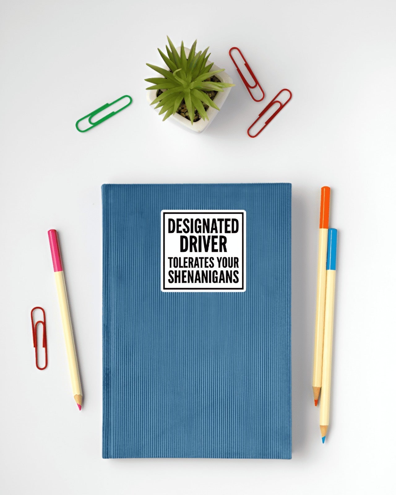 Blue notebook with a humorous sticker on a white surface with stationery items.