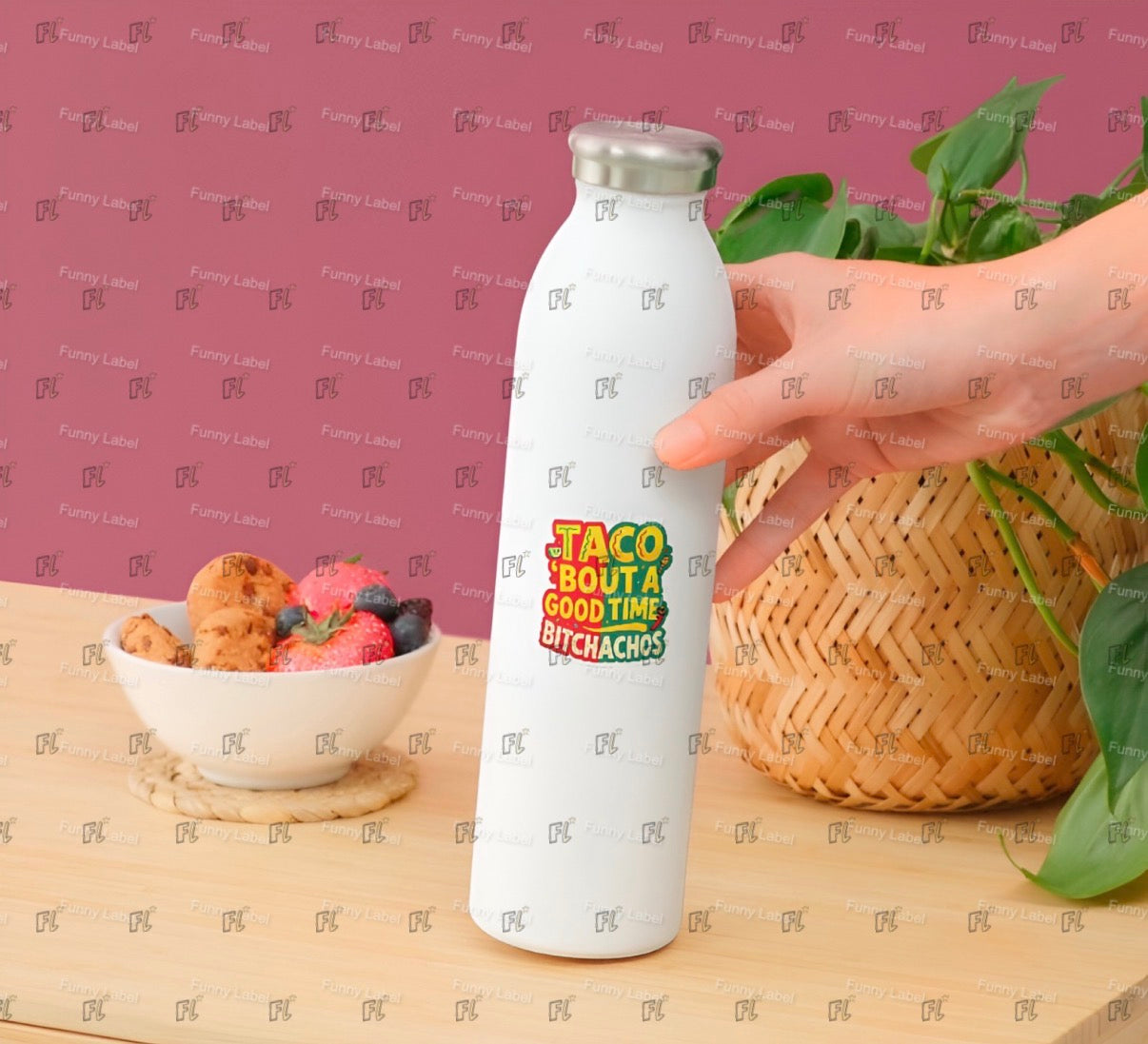 White water bottle with colorful text design held by a hand on a wooden surface with a bowl of snacks and a plant.