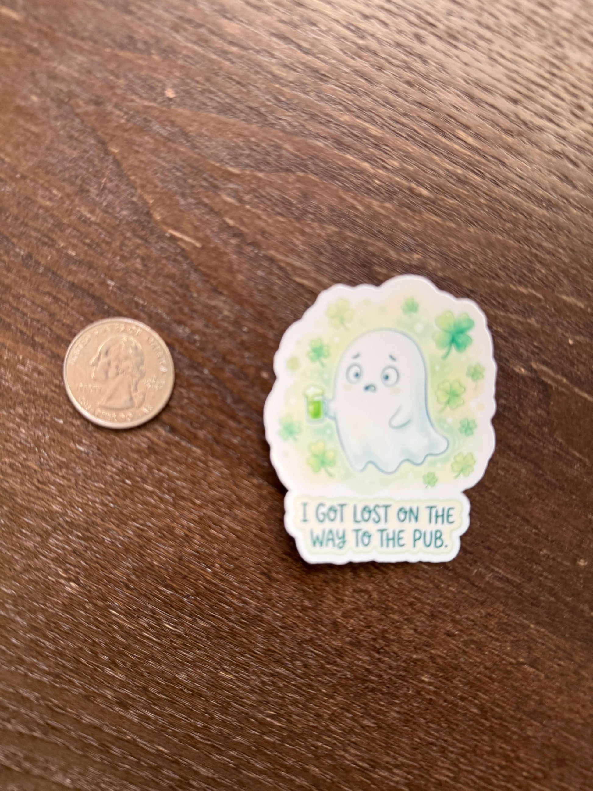 Sticker with a cat illustration and text on a wooden surface next to a coin for scale.
