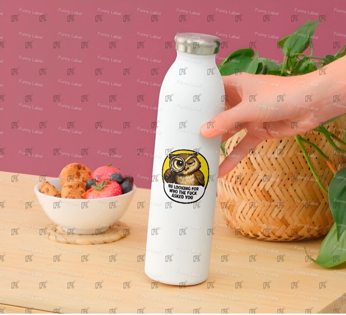 White water bottle with a sticker featuring an owl design, held by a hand on a table with a bowl of fruit and a plant.