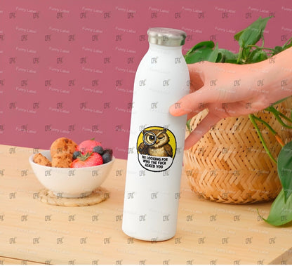 White water bottle with a sticker featuring an owl design, held by a hand on a table with a bowl of fruit and a plant.