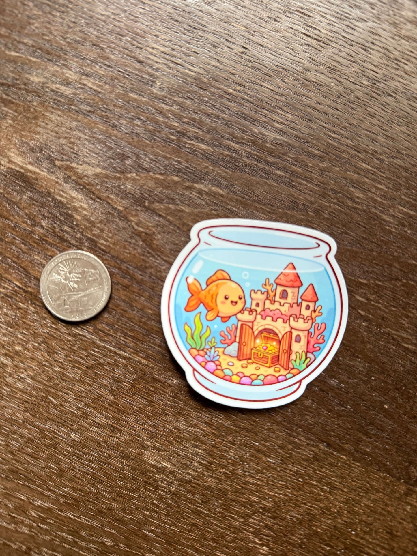 Sticker of a fish and castle design on a wooden surface with a coin for scale.