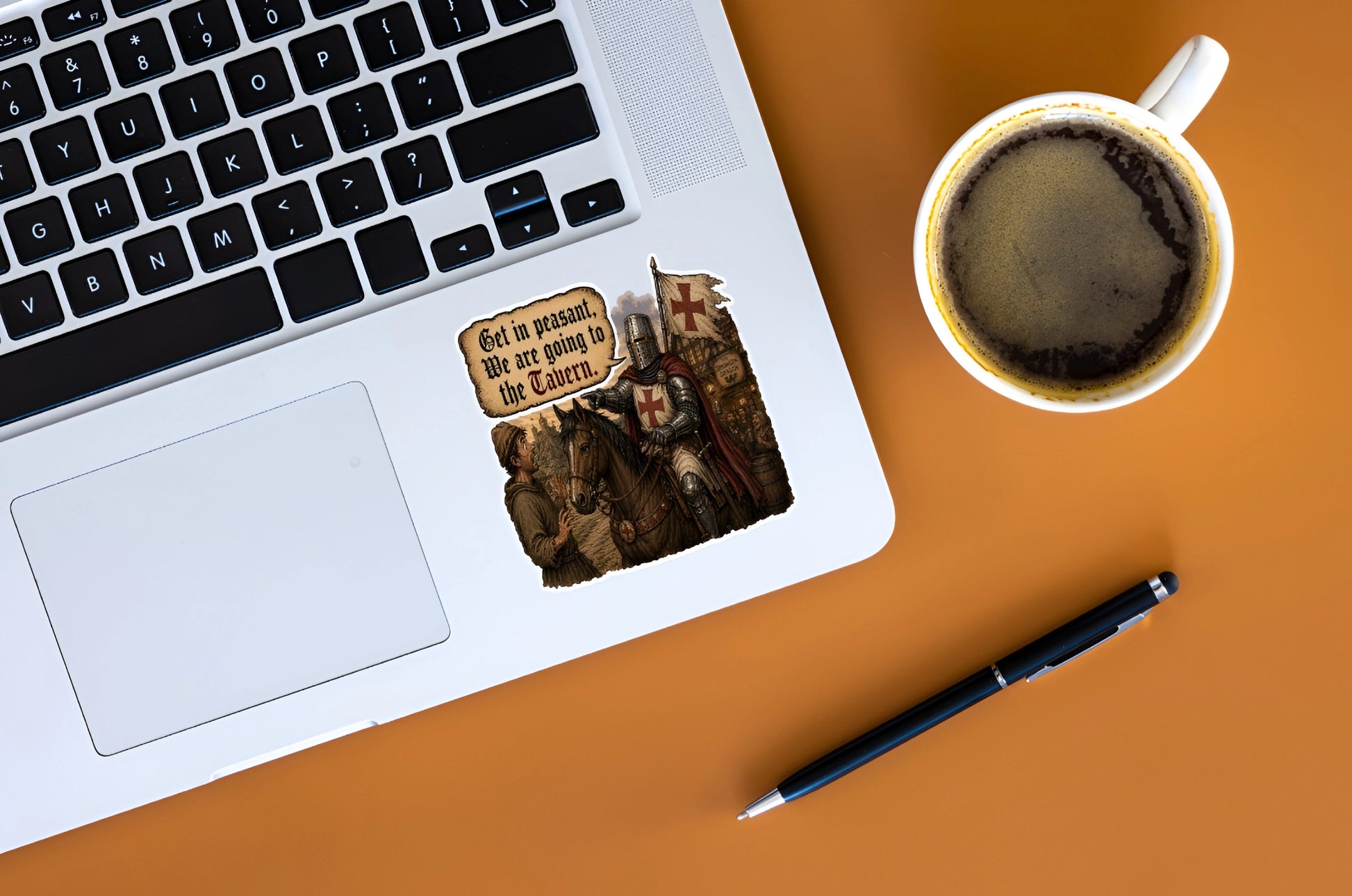 Funny tavern knight sticker with Get In Peasant quote displayed on a silver laptop beside coffee
